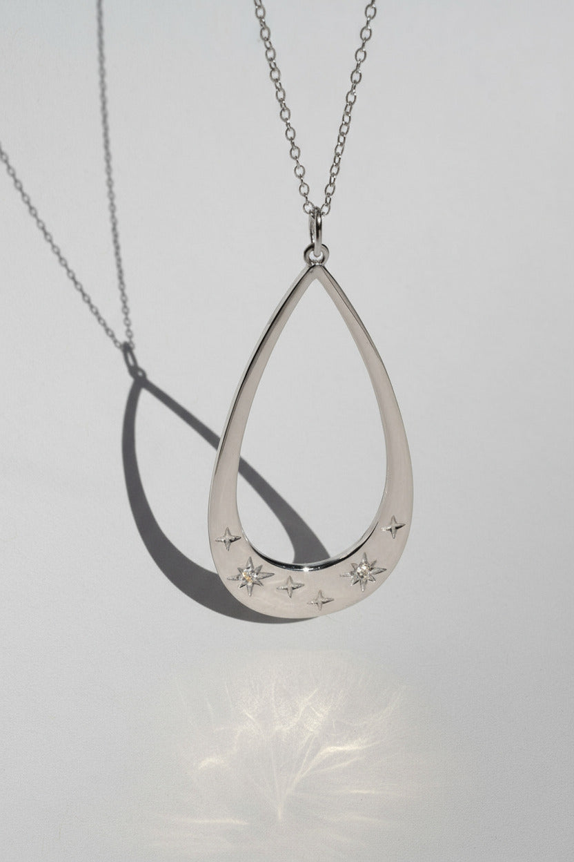 Silver teardrop-shaped pendant with star designs on a light gray background