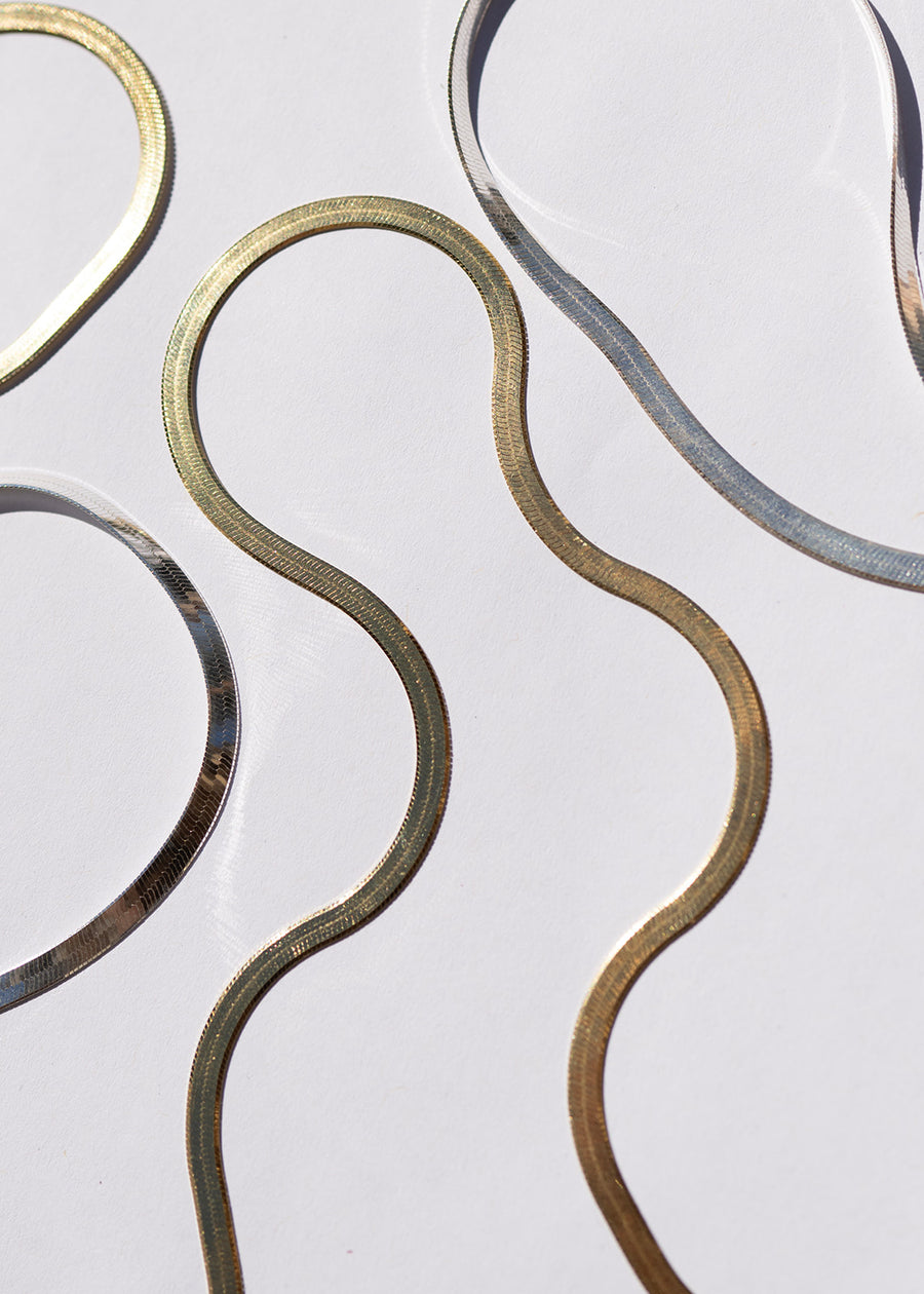 Decorative metal wall art with wavy patterns in gold, silver, and bronze on a light gray background.