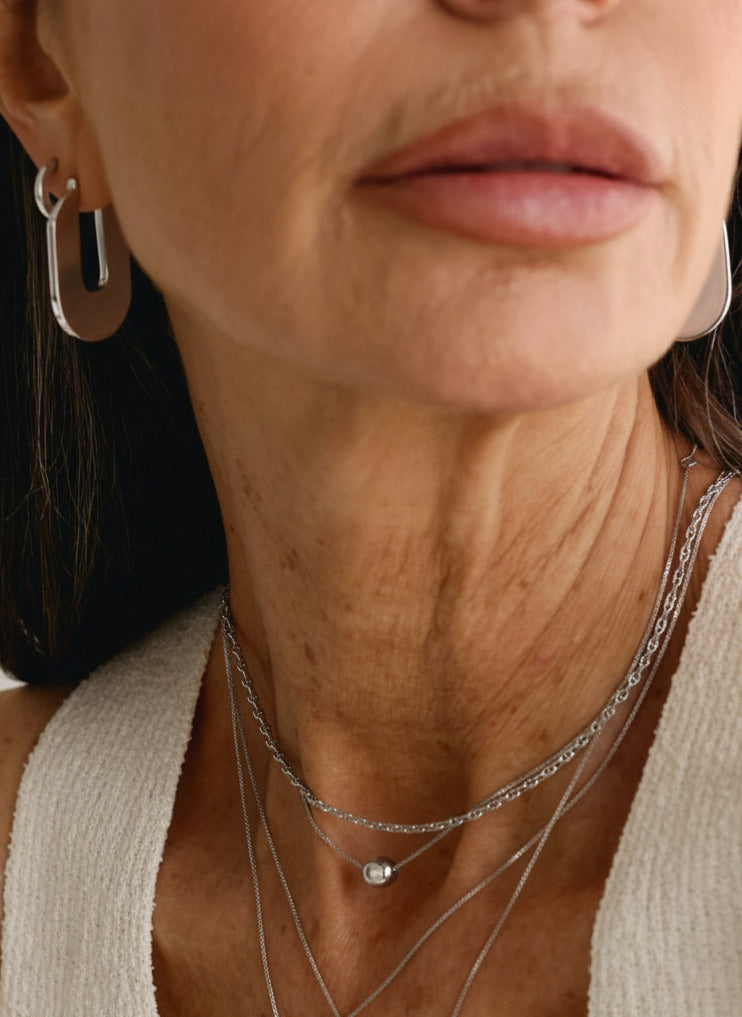Close-up of a person wearing silver earrings and necklaces.