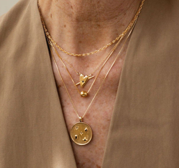 A close up photo of a woman wearing a layer of gold necklaces by designer Sarah Mulder