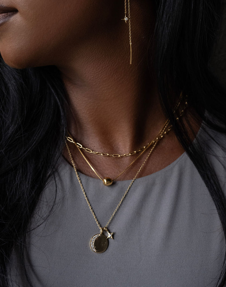 Close-up of a person wearing gold necklaces with pendants on a dark background