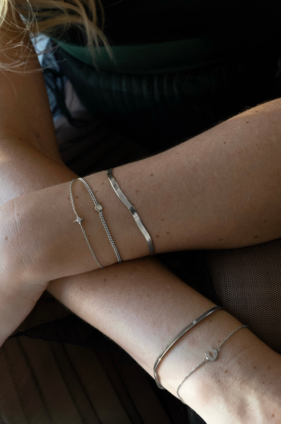 Close-up of a person's arms with silver bracelets on a dark background