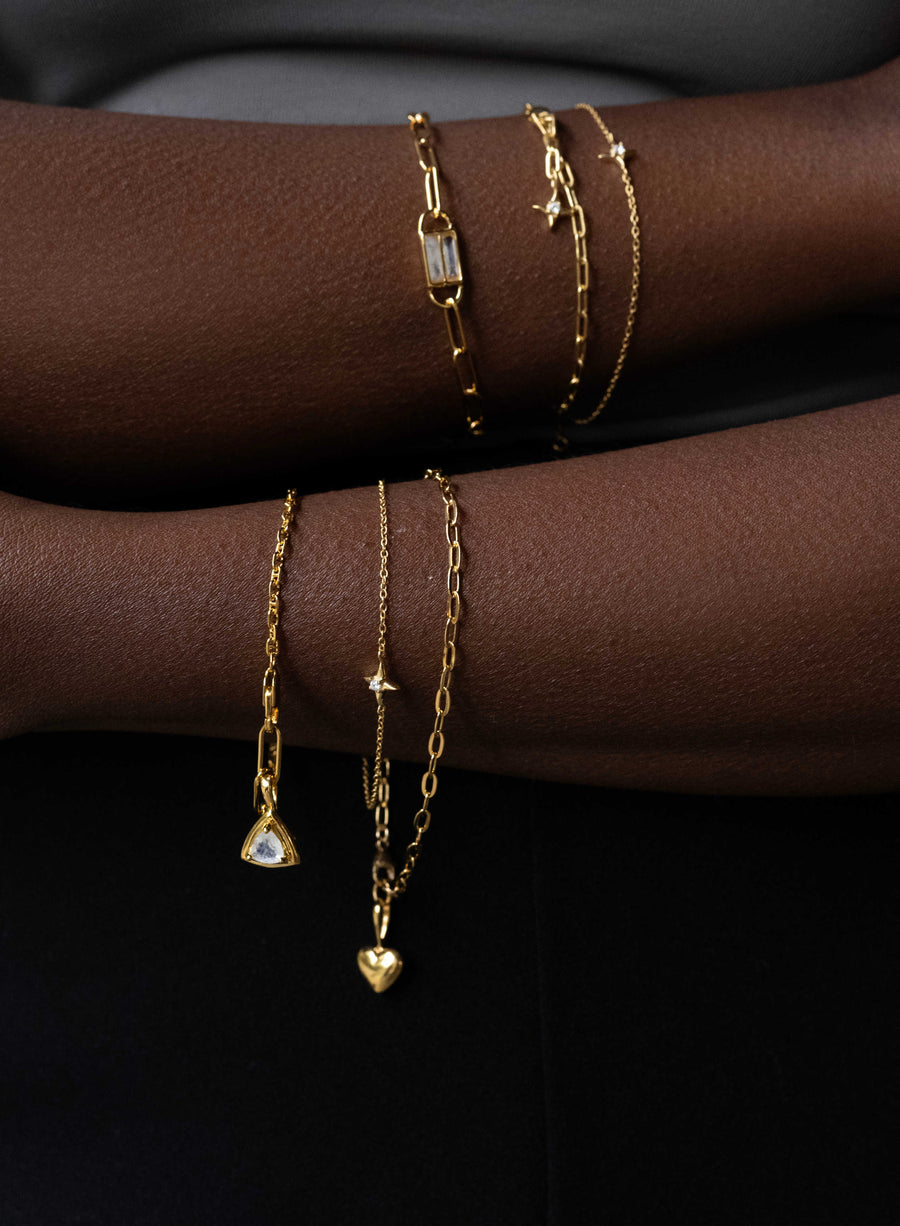 Gold bracelets and necklaces on a person's wrist against a dark background