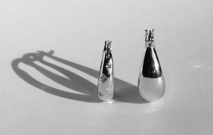 two hoops side by side one has small stars etched on it the other is a teardrop shape earring