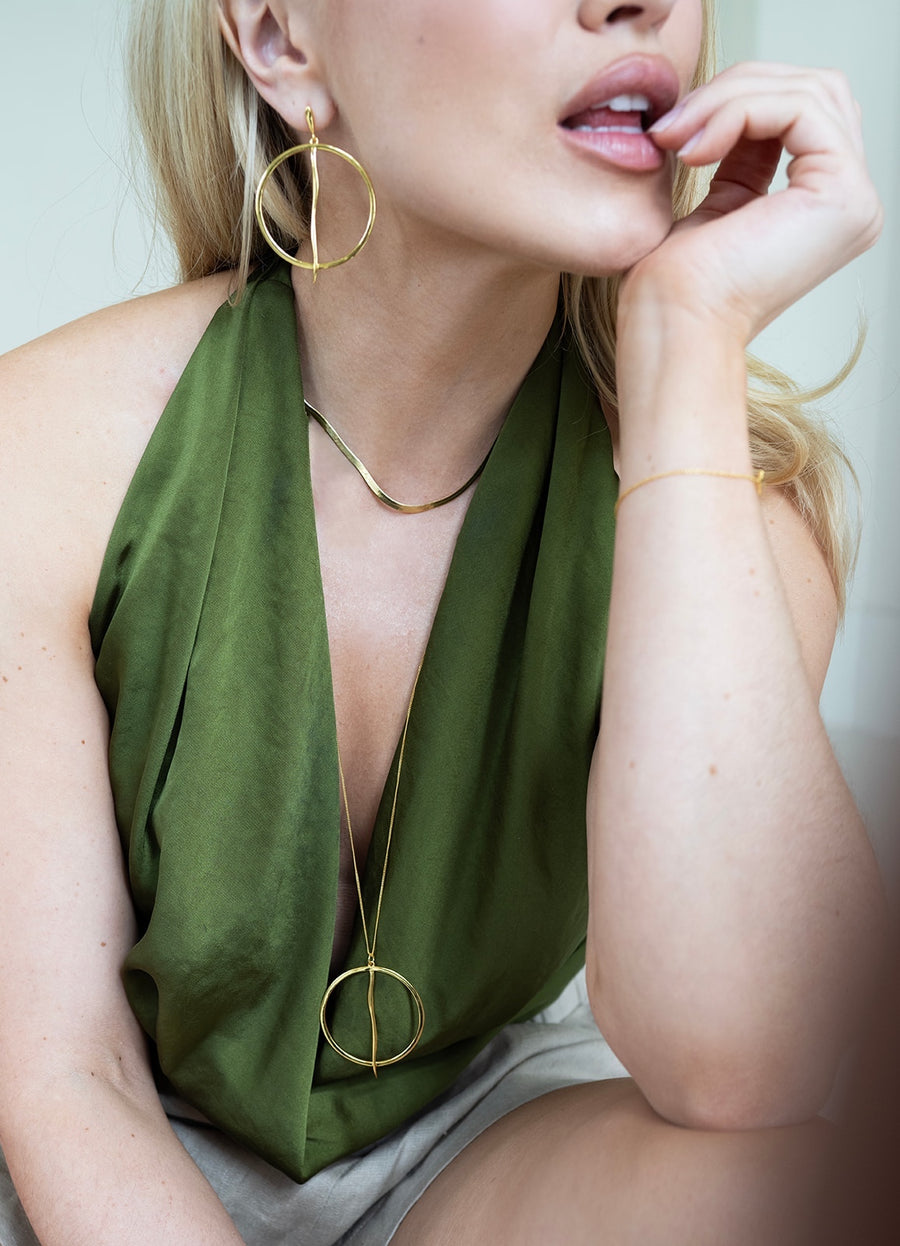 Woman wearing gold hoop earrings and necklaces against a neutral background
