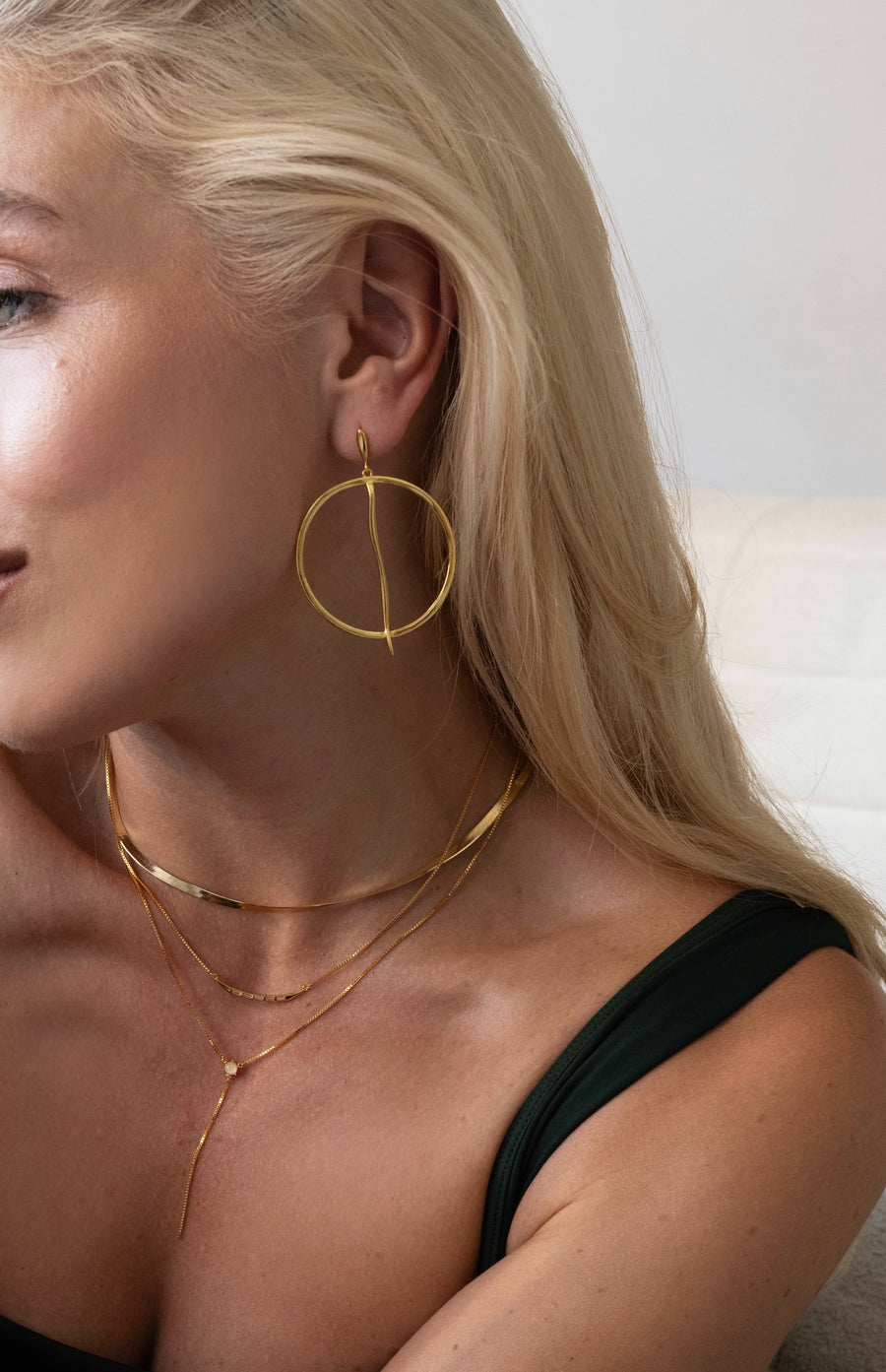 Woman wearing gold hoop earrings and necklaces against a neutral background