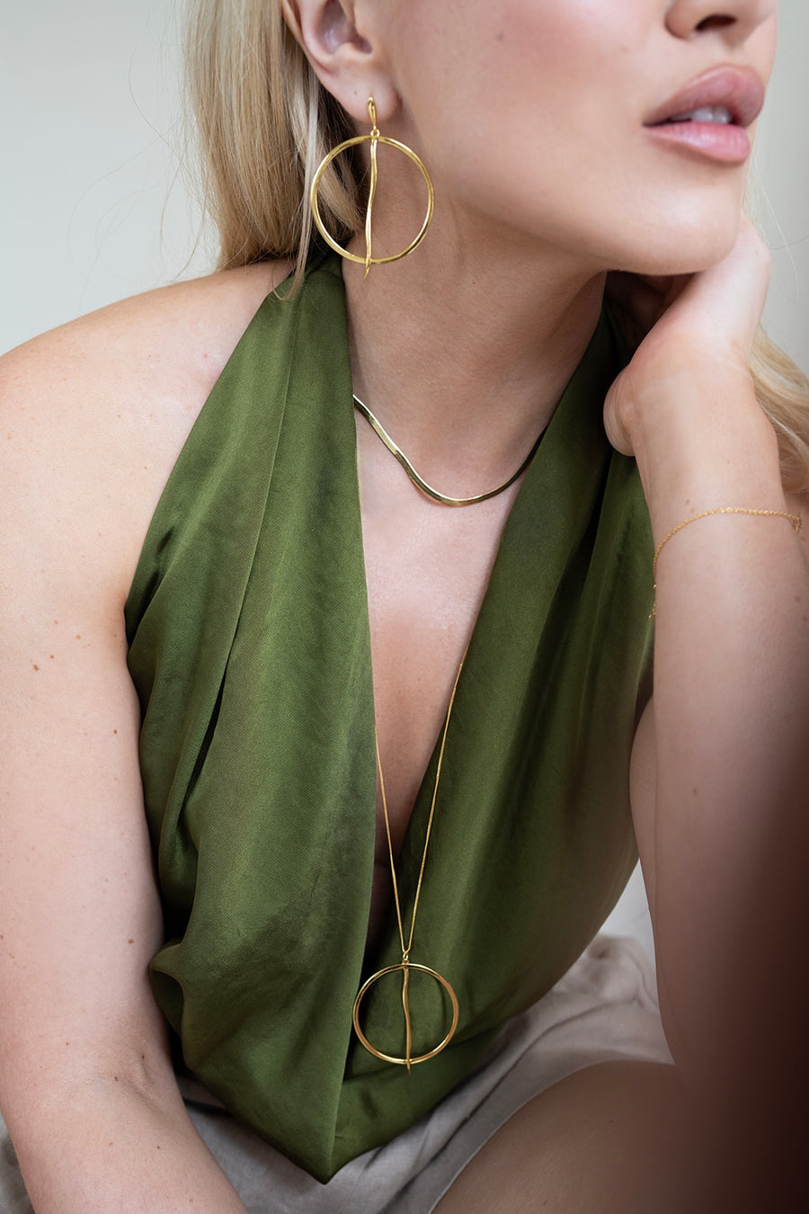 Woman wearing gold hoop earrings and a long gold necklace with a green top.