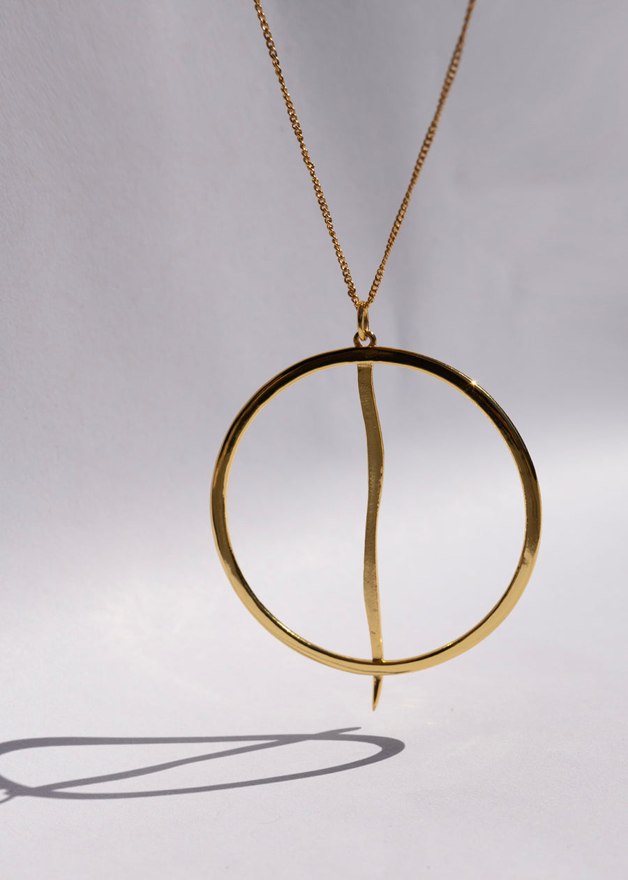 Gold necklace with a circular pendant on a gray background