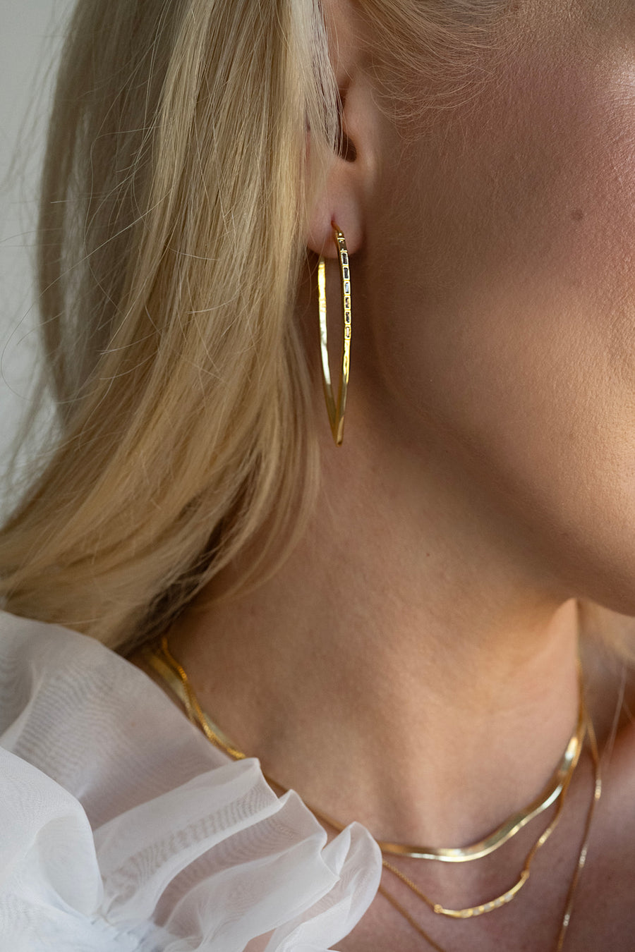 Close-up of a person wearing gold hoop earrings and a gold necklace.