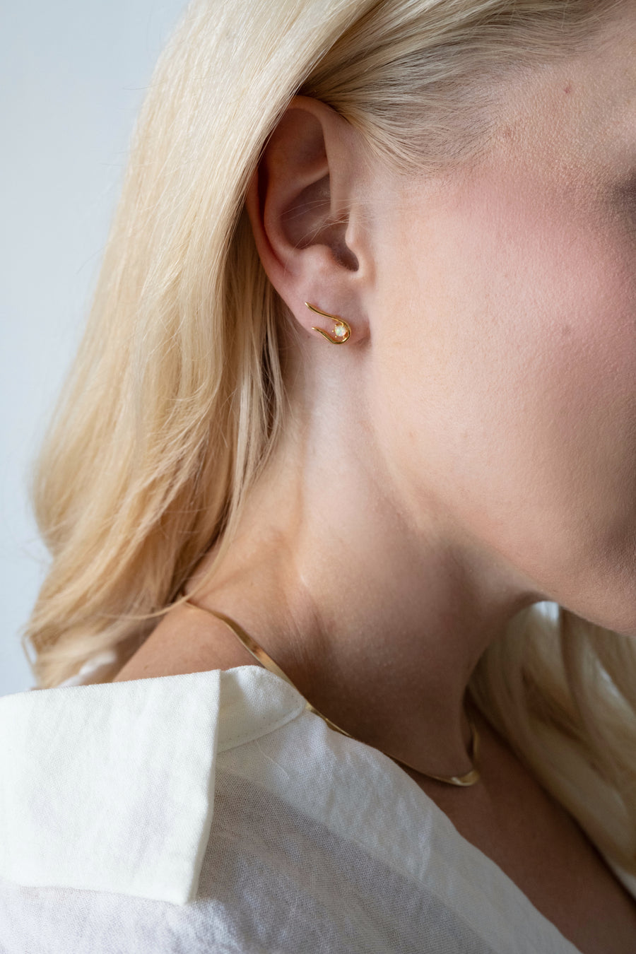 Close-up of a person wearing a gold earring with a plain background