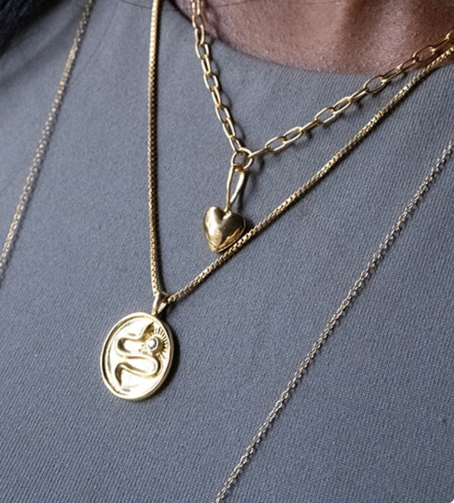 two gold necklaces worn in a layer, one is a puffy heart necklace and the other is a snake coin pendant necklace