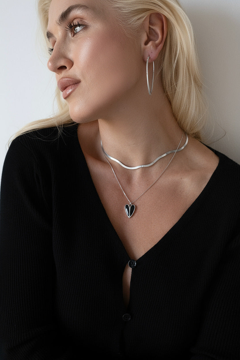 Woman wearing a silver necklace with a heart pendant against a neutral background