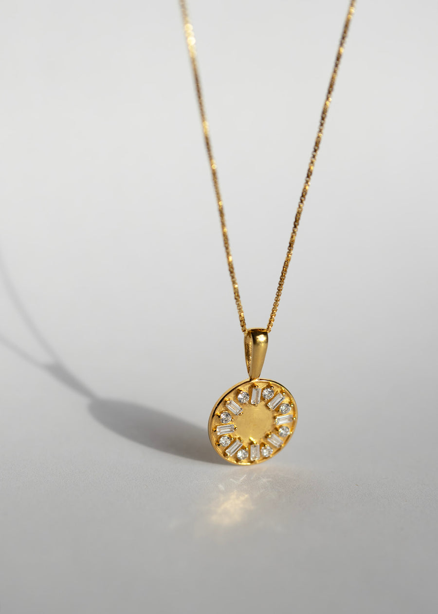 Gold necklace with a round pendant on a light gray background