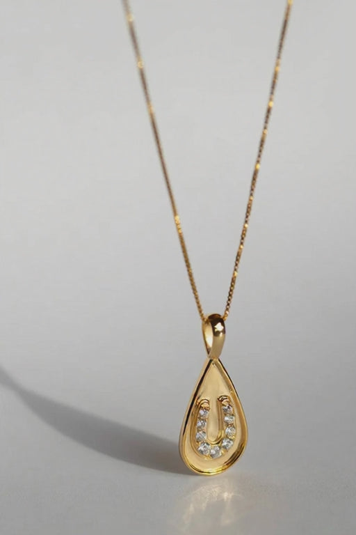 Sarah Mulder Jewelry Horseshoe necklace in gold on a grey background casting shadows as it moves