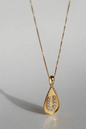 Sarah Mulder Jewelry Horseshoe necklace in gold on a grey background casting shadows as it moves