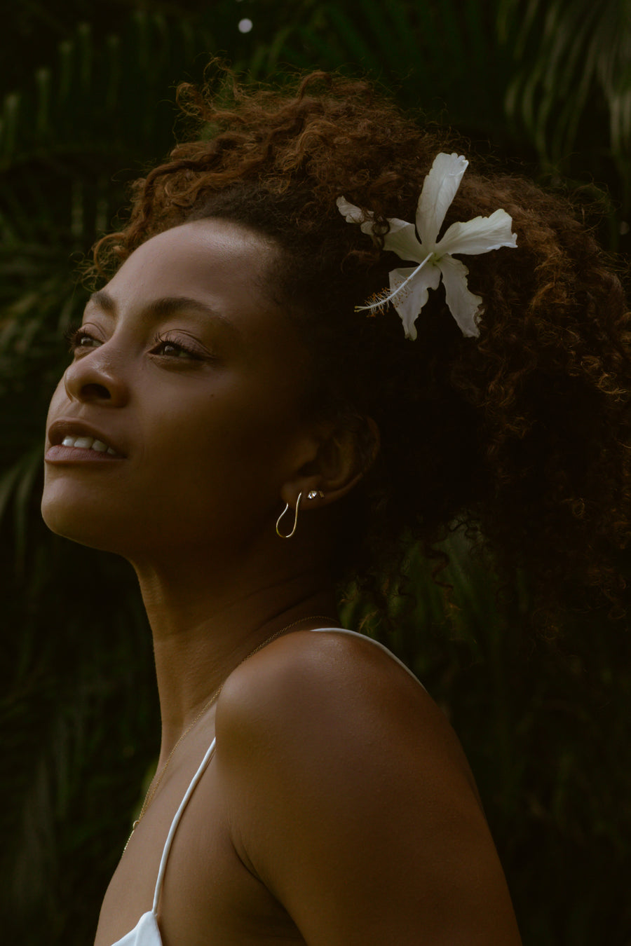a model with a flower in her hair wearing a fluid shaped earring