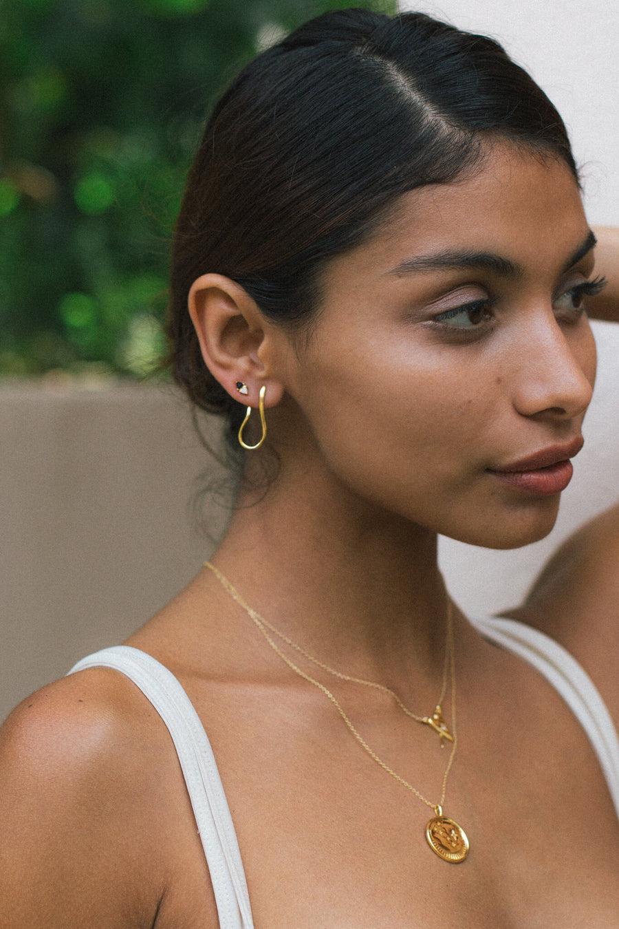 woman standing with earrings and necklaces on in a tropical setting
